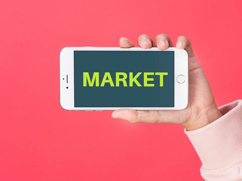 A hand holding a phone displaying the word MARKET on a pink background